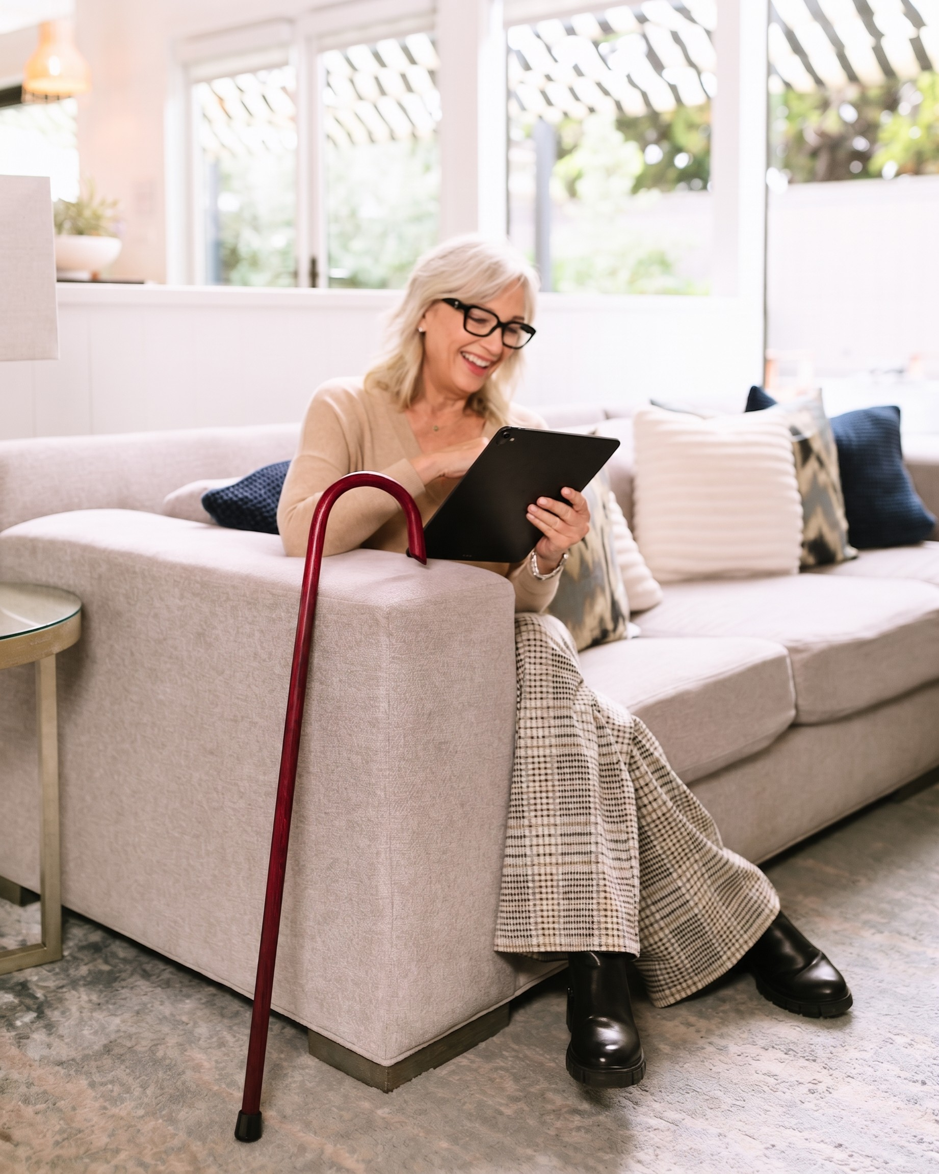 Woman sitting on a couch holding a tablet with a crimson 7/8" Classic American Walking Cane beside her